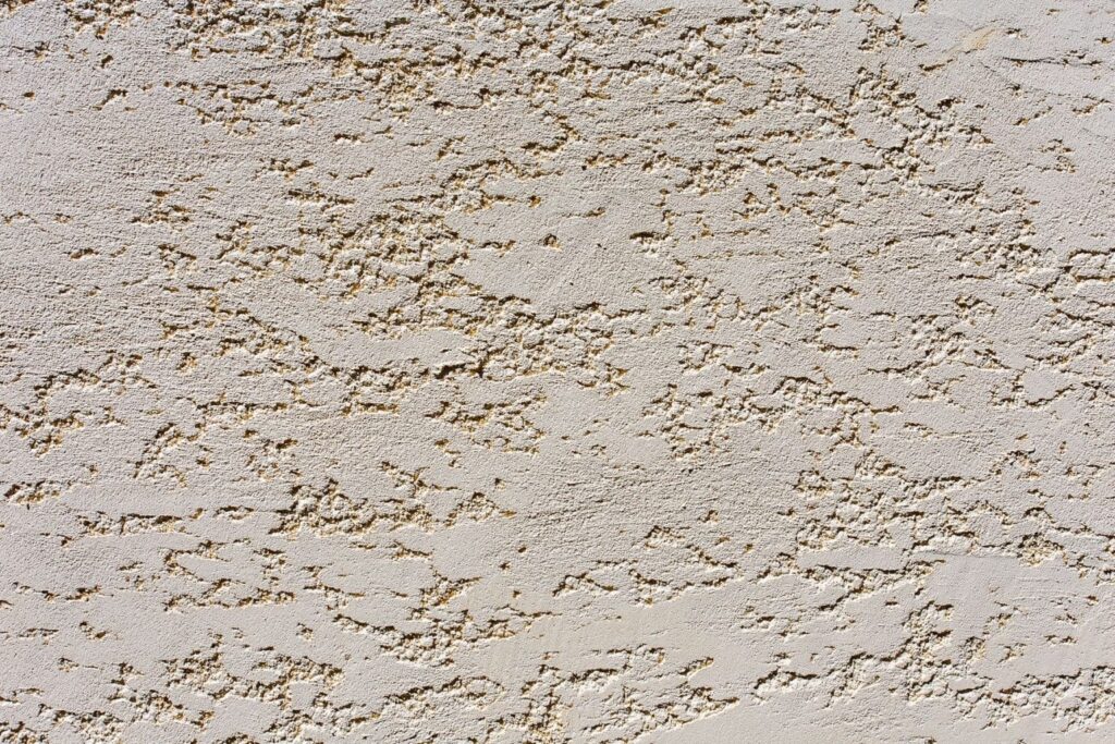 Finition de façade en enduit grain écrasé, avec surface partiellement lissée laissant apparaître une texture légèrement granuleuse.