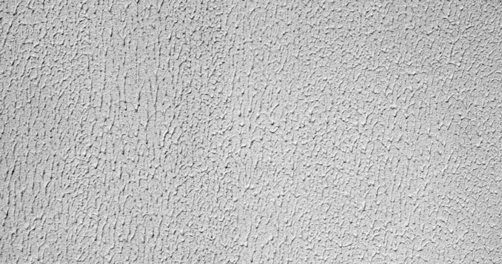 Gros plan sur une finition de façade en enduit grain projeté, avec texture granuleuse et irrégulière caractéristique.