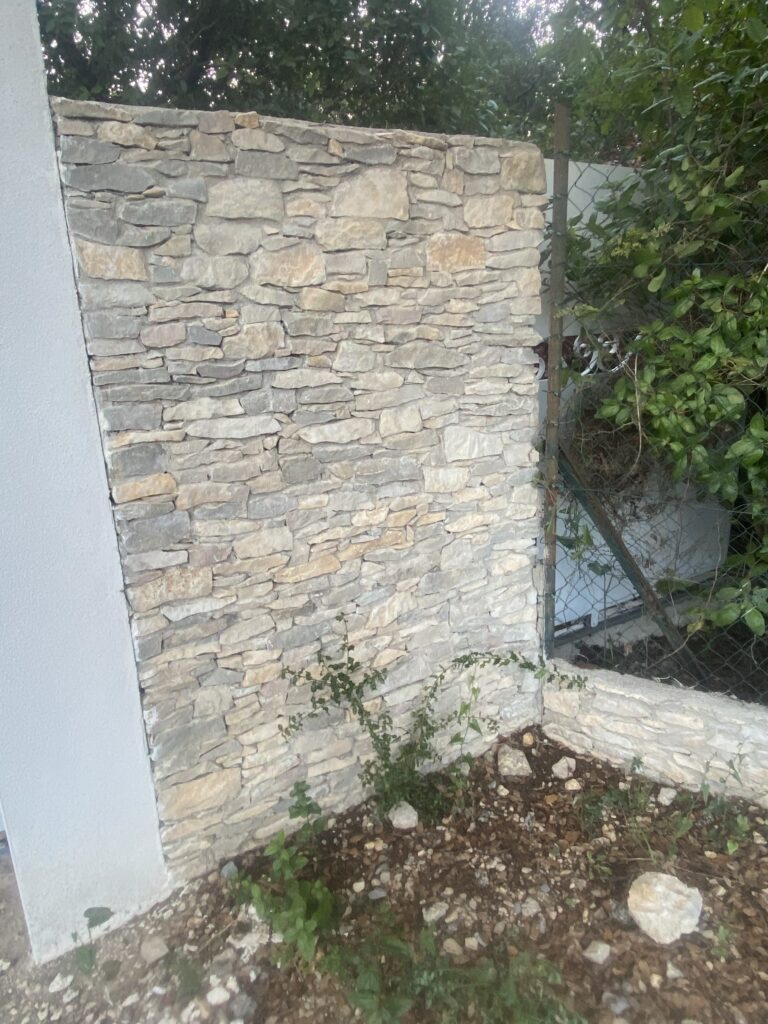 mur en pierres naturelles a côté d'un pilier construit en cairon terminé en facade finition grattée.